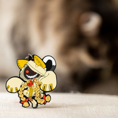 Image showcasing the Taokaka keychain, a piece of Blazblue merchandise, with a background featuring a furry, creamy cat.