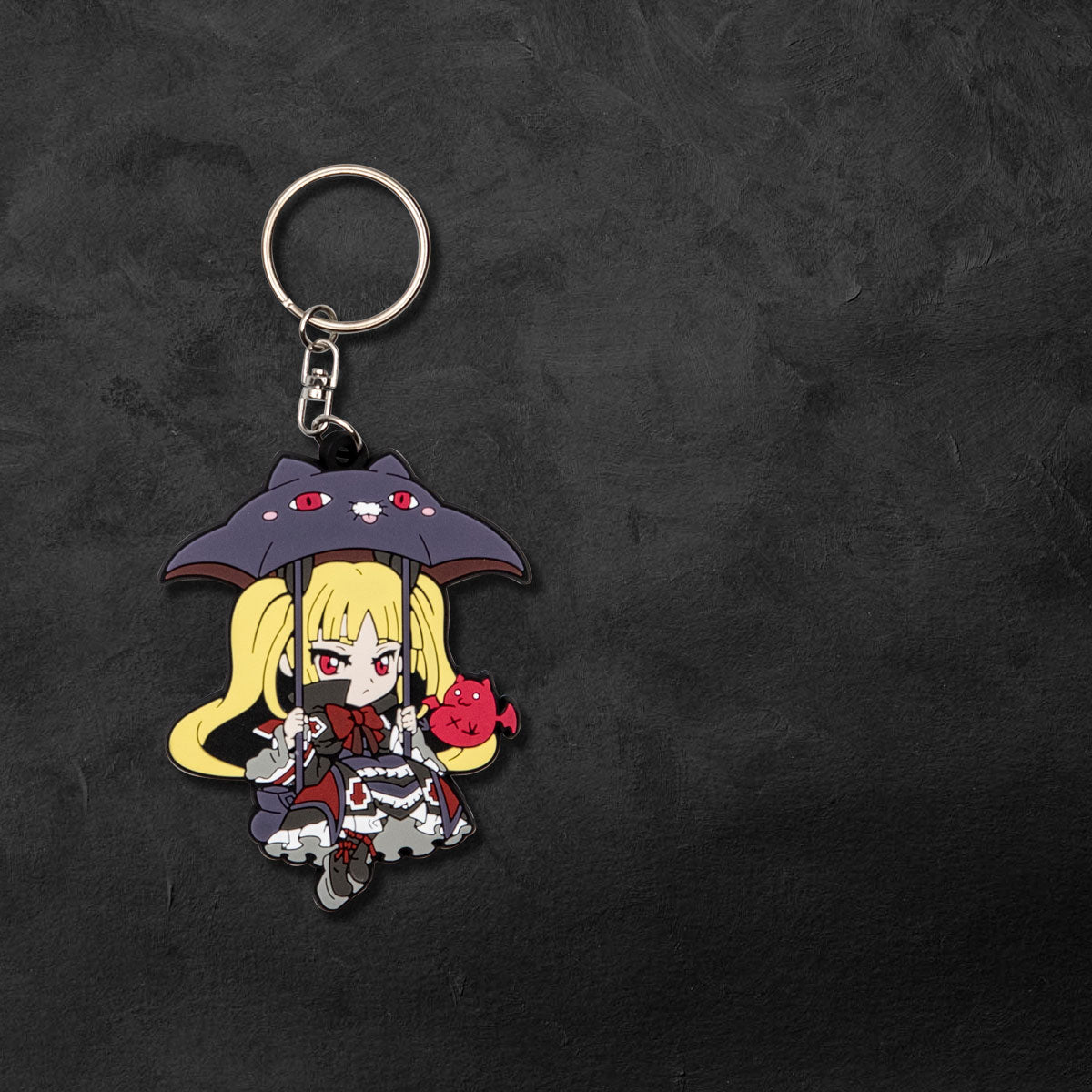 The official Blazblue Rachel Alucard keychain by Eighty Sixed. Flat lay on a dark charcoal background. Chibi Rachel.