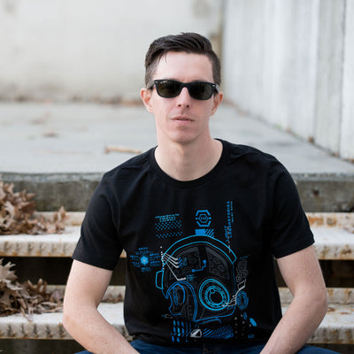 This photo shows a man wearing the Mega Man Diagnostic shirt. He is sitting on metal stairs with cement behind him that is nicely blurred.