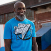 A photo of a man wearing the Mega Man Dr. Wily tee by Eighty Sixed. He has a big smile, and is standing in an open air market that is nicely blurred in the background.