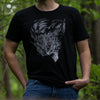 This image is a closeup shot of a young man wearing the Monster Hunter Elder Crossing tee. He has one hand in his pocket, and is standing in a dark forest with a nice blurred background.