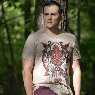 A photo of a man in a forest wearing the Monster Hunter Odogaron shirt. He is in shadow, but there are rays of light that illuminate the shirt design.