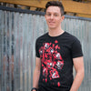 A photo of a man wearing the Persona 5 All Out Attack tee. He is standing in front of a metal wall that is nicely blurred.