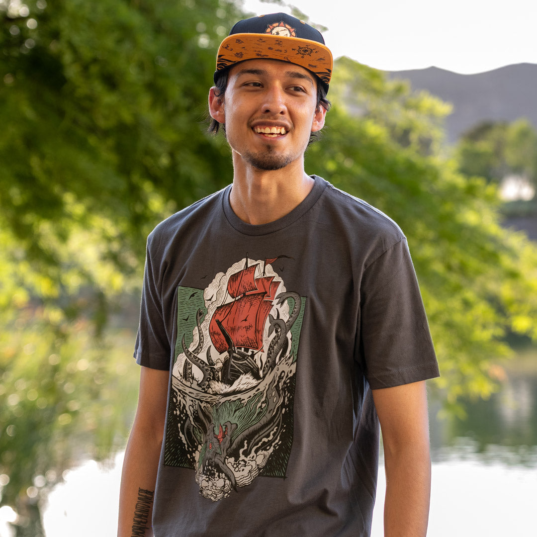 Man wearing the Sea of Thieves Kraken T-Shirt paired with the Sea of Thieves Reaper's Mark Snapback