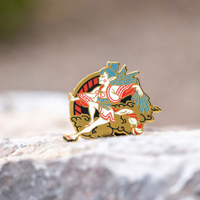 The Shin Megami Tensei V Amanozako pin is shown on a rock, with a beautiful blurred background.