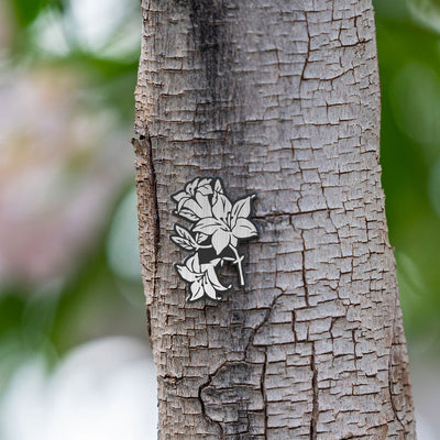 The Jouin Satsuki pin is sitting on a tree branch surrounded by beautiful green leaves.