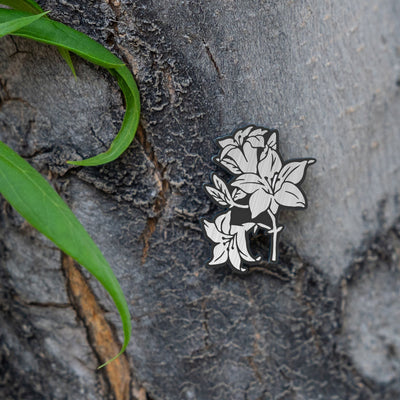 The Jouin Satsuki Shin Megami Tensei V pin is shown on bark with other green plants around it.