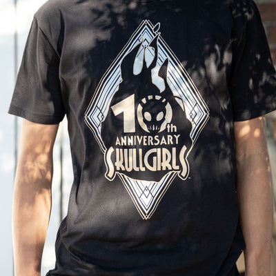 The photo shows a closeup of the Skullgirls 10th Anniversary shirt. It has sunlight peaking through some trees highlighting the design.
