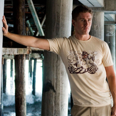 Photo of a man wearing the Street Fighter Chest Slap shirt. He is standing under a boardwalk leaning on one of the pillars.