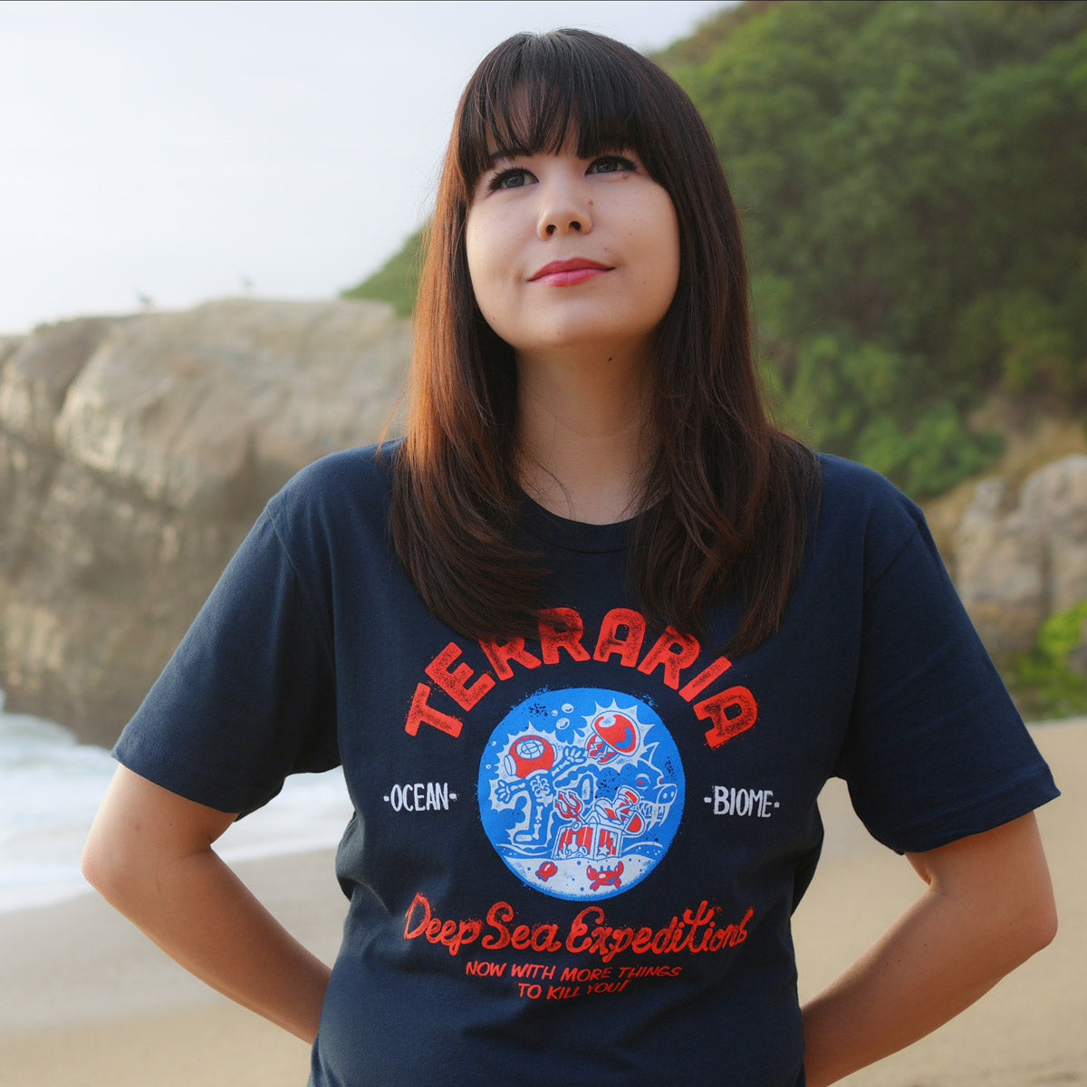 Model wearing the Terraria Ocean Biome T-Shirt featuring the text "Deep Sea Expeditions - Now With More Things to Kill You!"